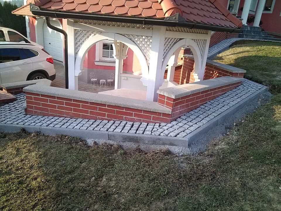 Tlakovana pot iz granitnih kock okoli nadstreška z urejeno zelenico